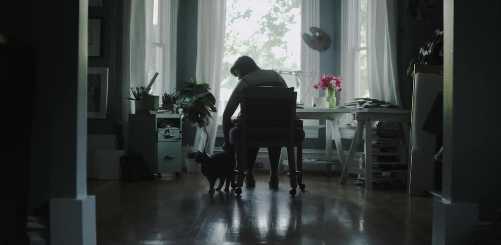 A woman sitting in a chair bends over to pet a cat
