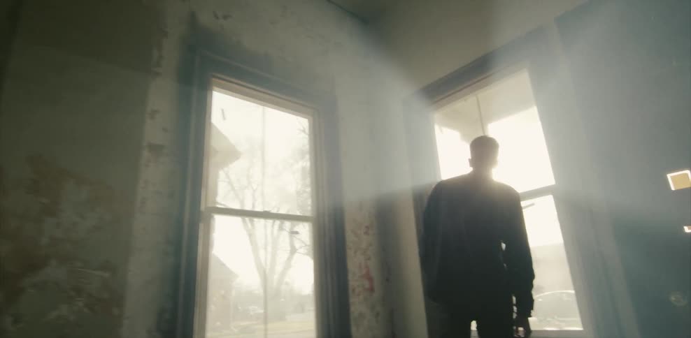 Man walking through an empty house to look out the window on a sunny day