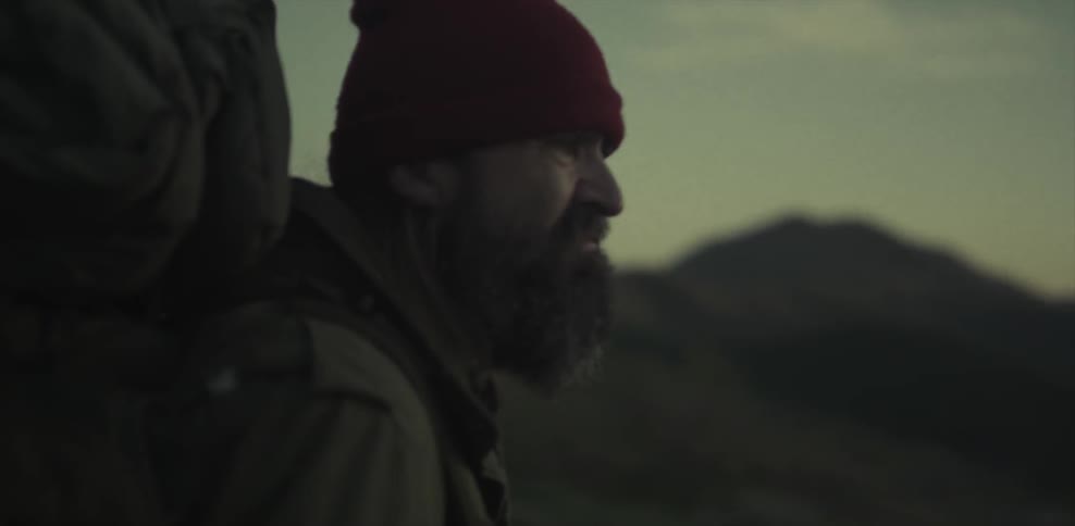 Man wearing a backpack looks out at hilly terrain