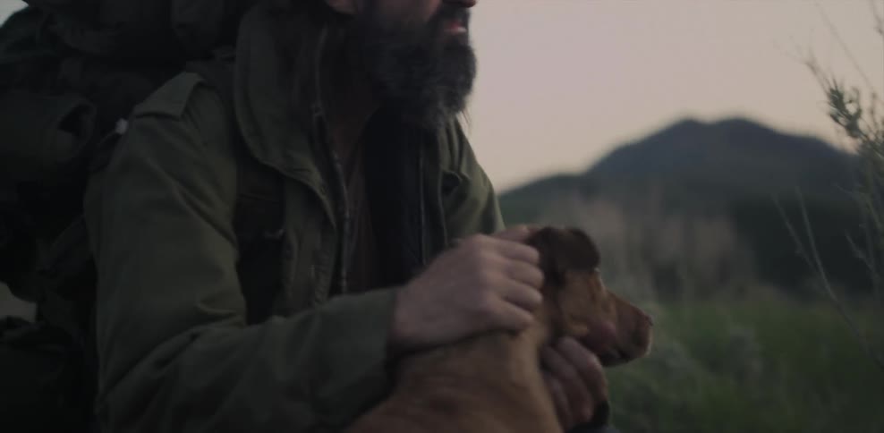 A man pets his dog while hiking