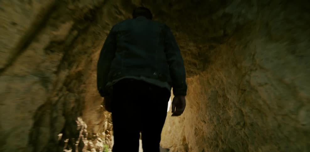 A man walks through a cavern towards an opening