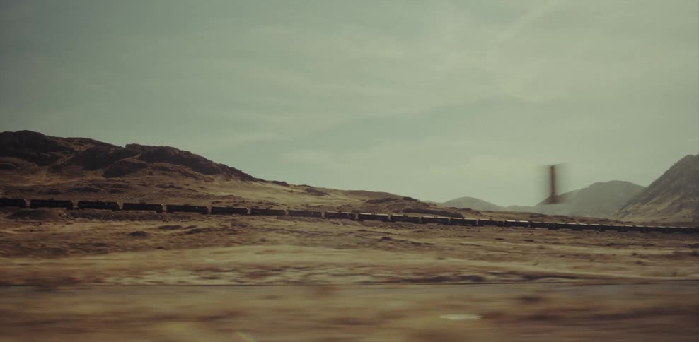 A train travels through a rural area with mountains in the distance