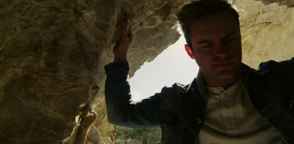 Man standing in a cave opening at sunset