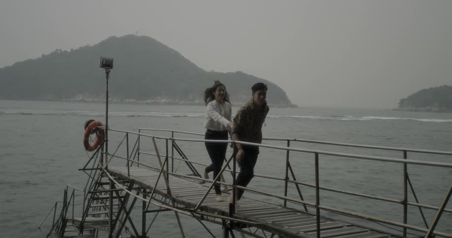 A man and woman hold hands while running on a pier