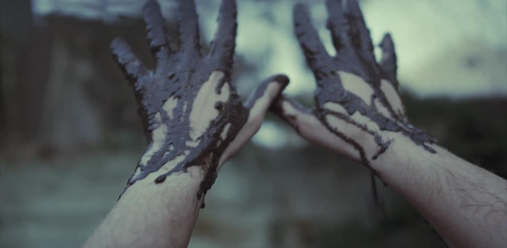 A person covers their hands in mud