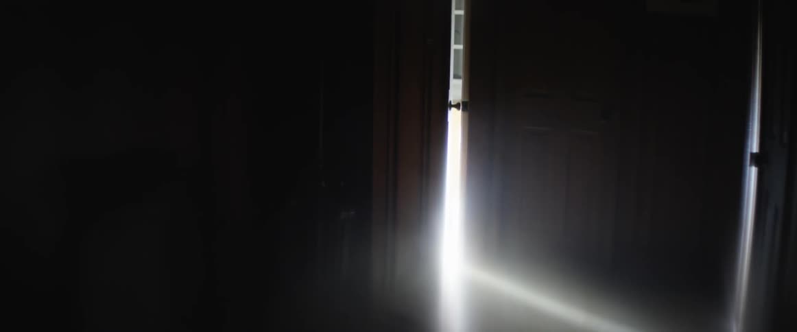 Light leaks through an ajar door into a dark room