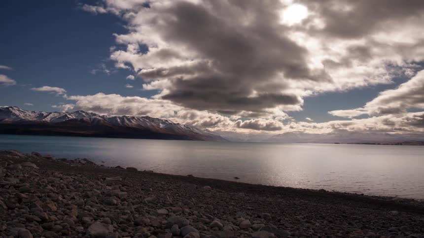 Clouds move over a beach and a body of water with backgrounds in the distance