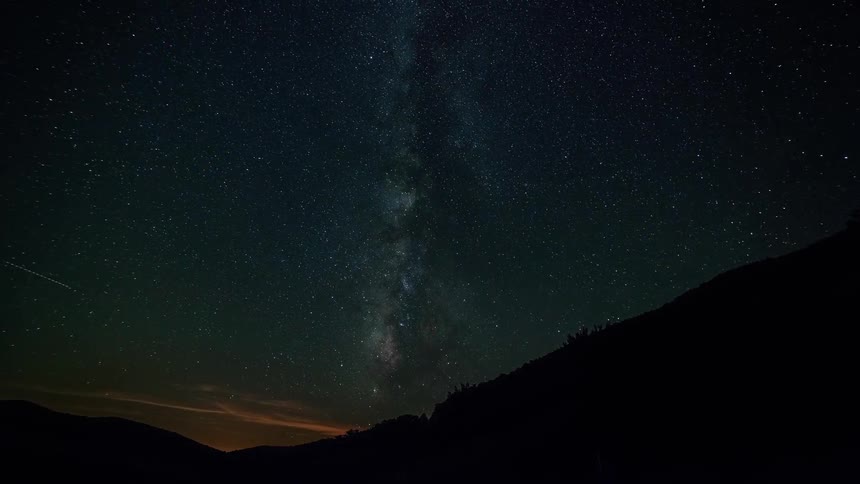 Timelapse of the night sky with two mountains in the foreground