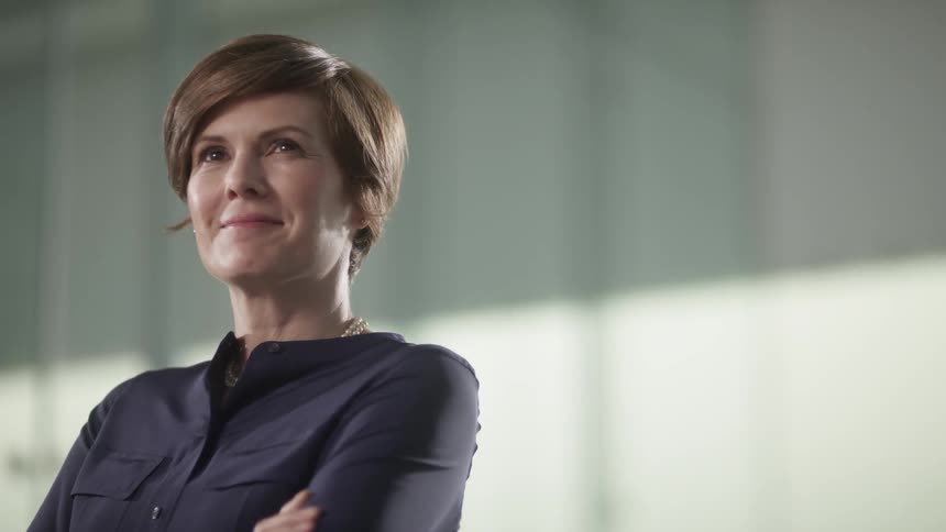 Woman grinning while standing stationary with her arms folded indoors
