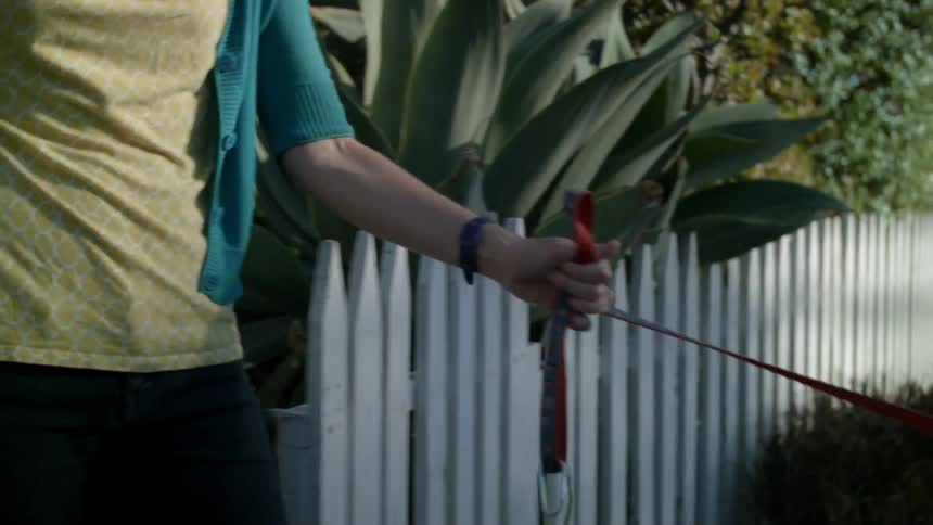 Woman opening a white picket fence gate with a leashed dog