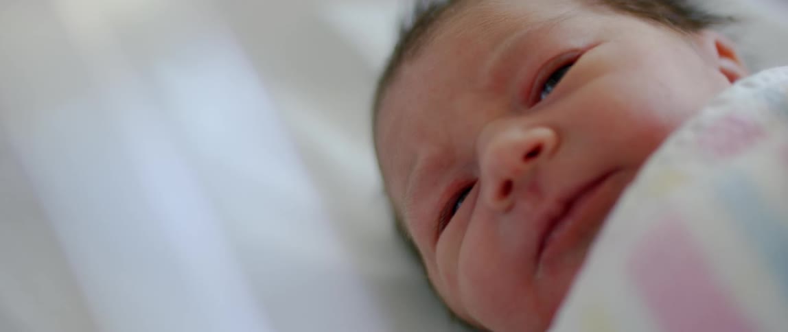 A baby lays in a blanket in the crib