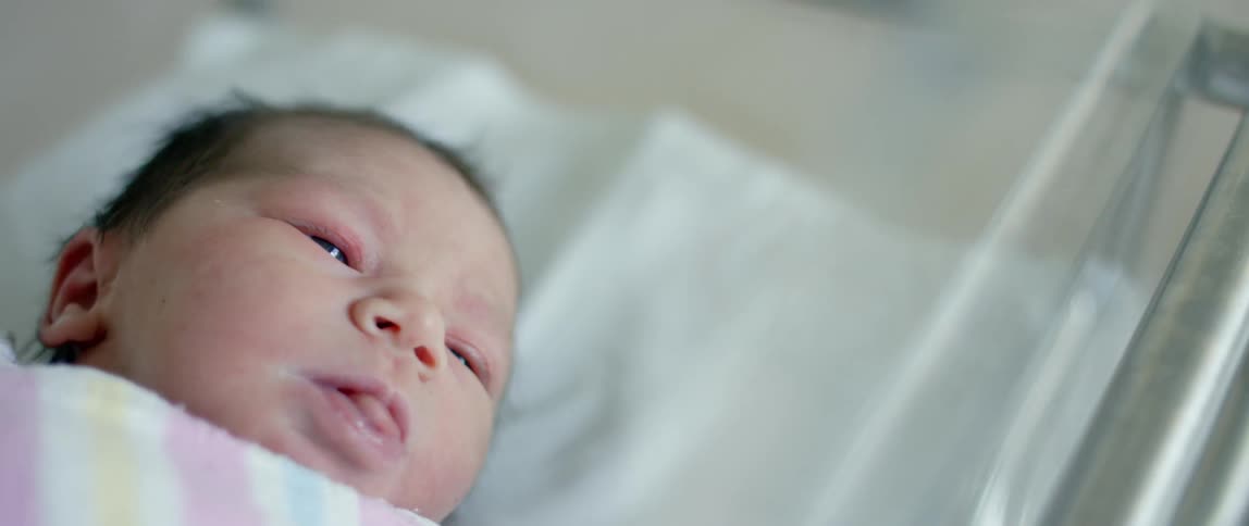 A newborn baby lies in a hospital crib