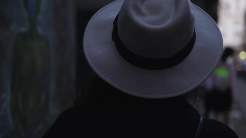 A woman wearing a hat walks down a city sidewalk