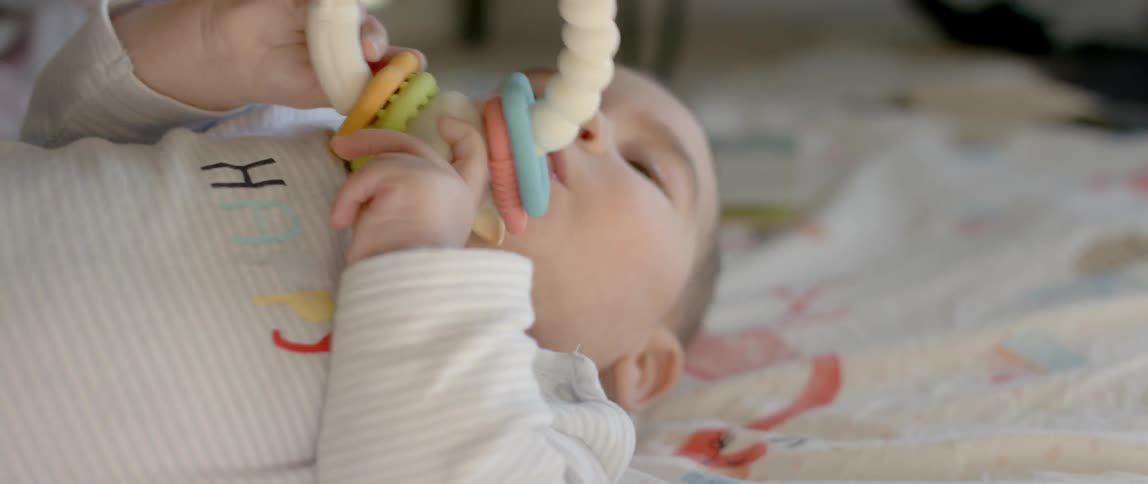 A baby is playing with and chewing on a rattle