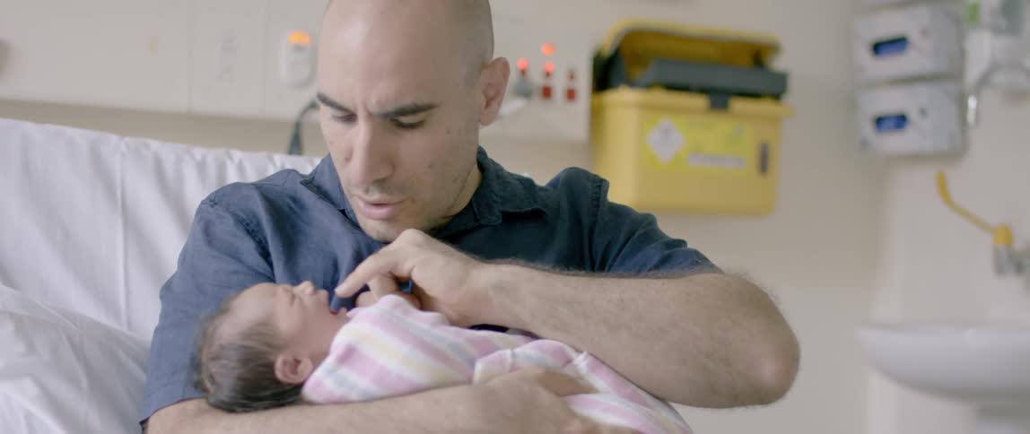 A man holds a swaddled newborn in the hospital