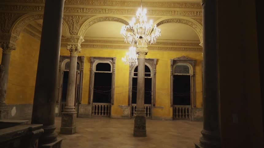 Lit chandeliers hang in a room at the end of a hallway