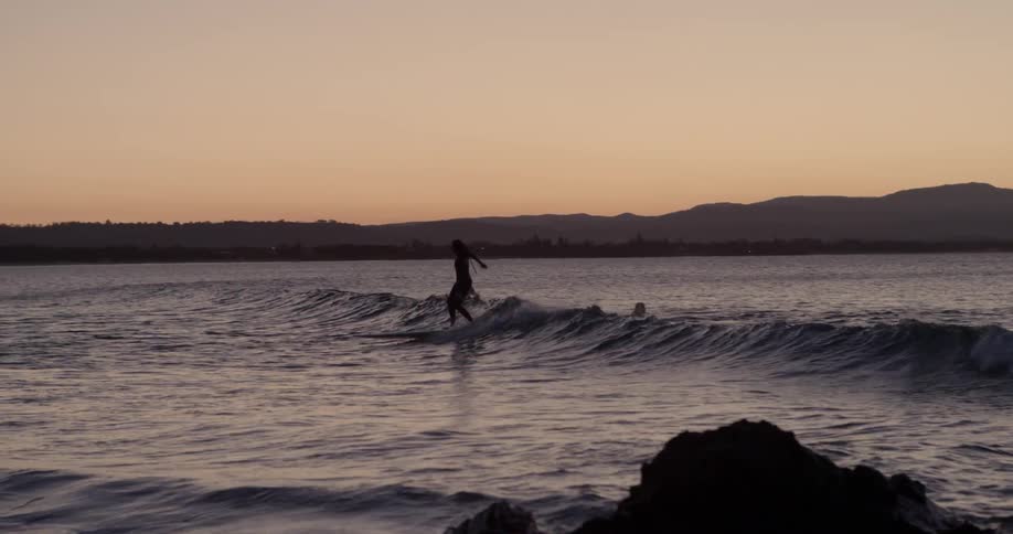 People surf near the coast at sunset