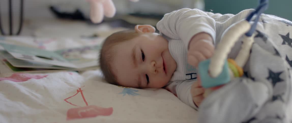 A baby lays on a blanket on the floor with baby toys