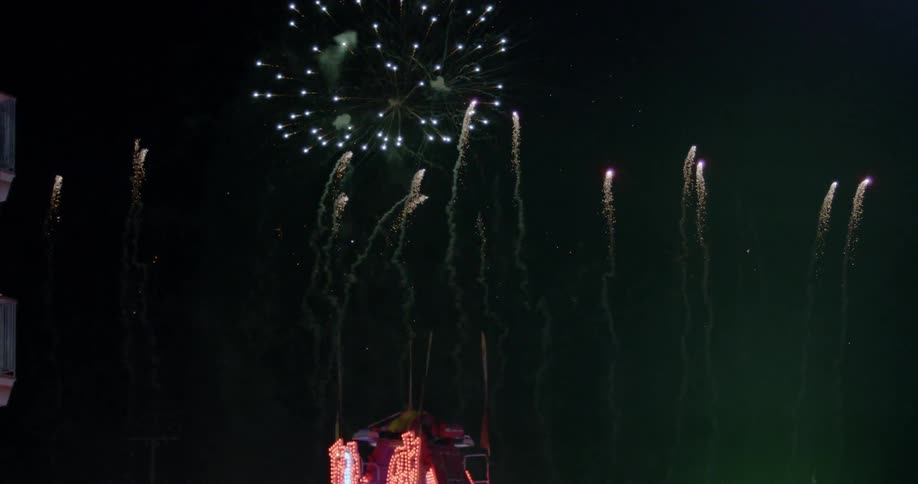 Fireworks explode behind spinning fair ride