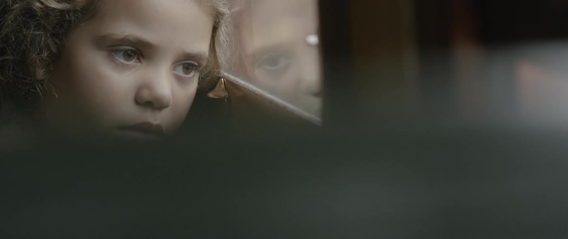 A tired little girl leans her head against the window in a moving train