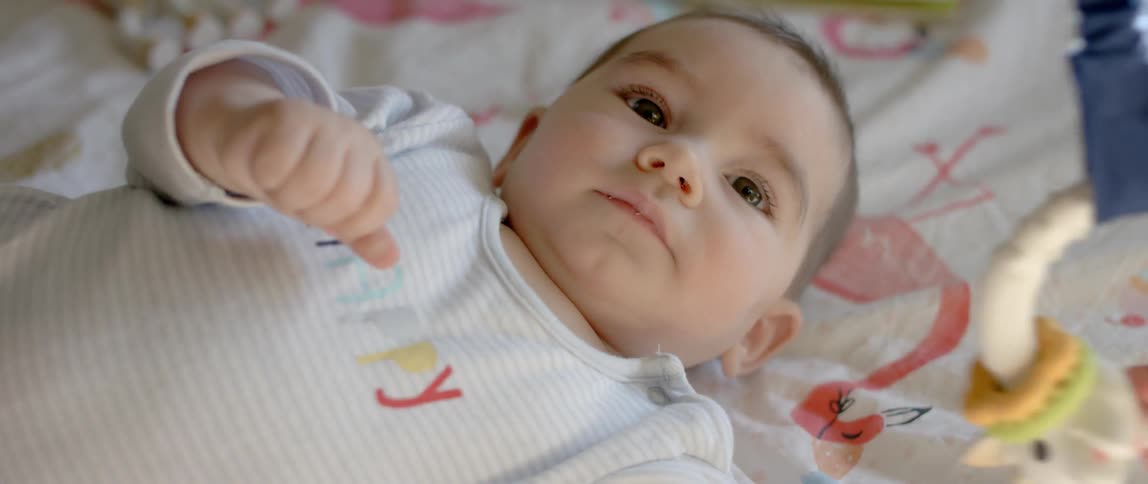 A teething ring hangs swaying in front of a baby lying awake on a blanket
