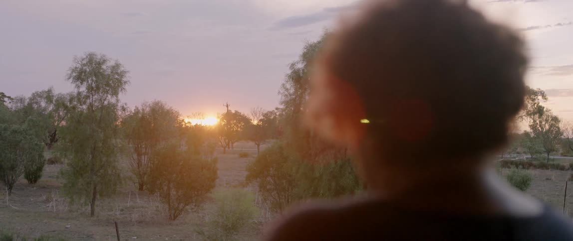 An older woman is watching the sun rise on the horizon