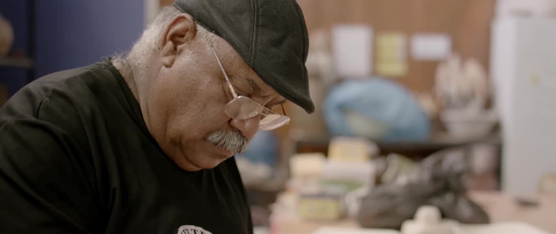 An older man is working on a ceramic plaque