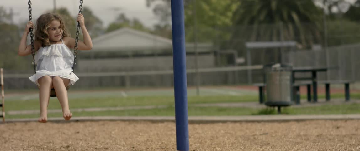 A little girl is playing on a swing in a playground