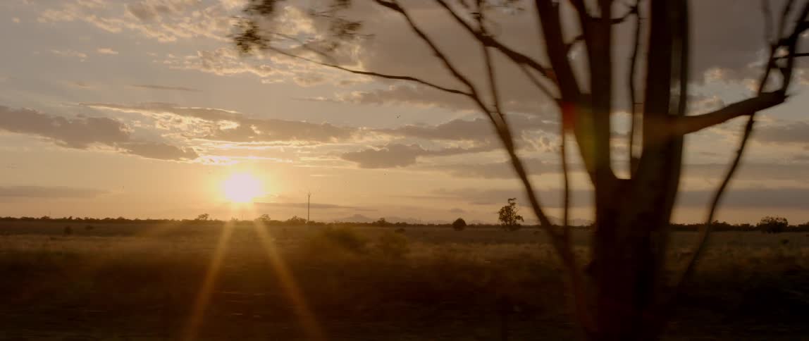 The sun rises over open fields in a cloudy sky