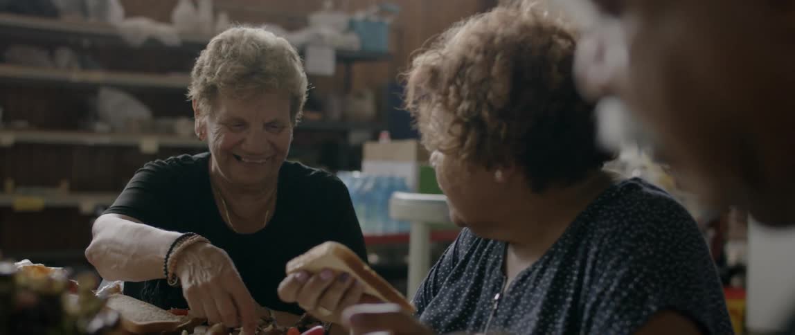 Two elderly ladies sit at a table eating and laughing