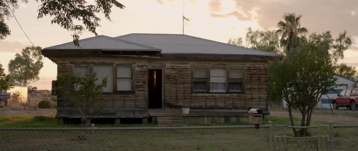 A dilapidated house is shown at sunset