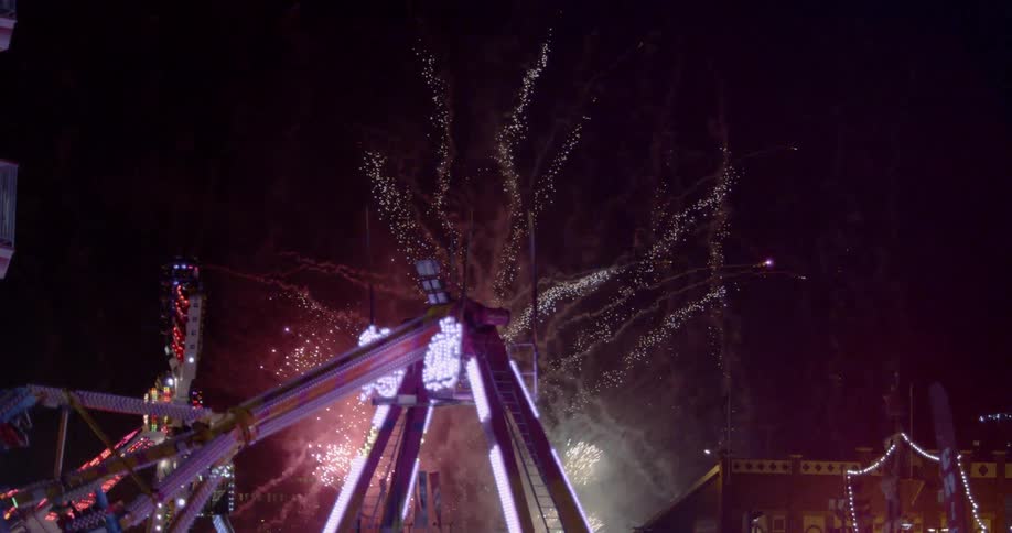 Fireworks explode behind spinning fair rides