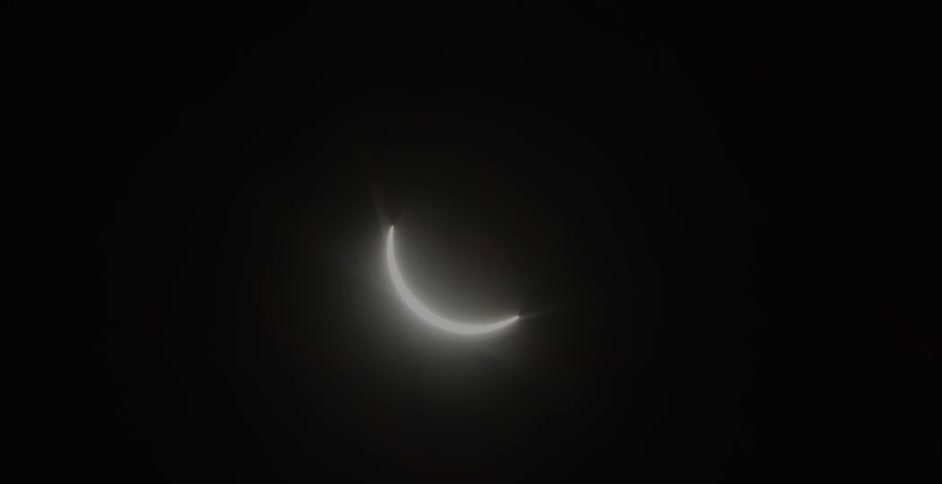 A crescent of light shines through the dark sky