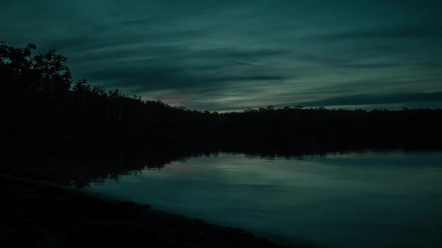 The sun sets above a lake as day turns into night
