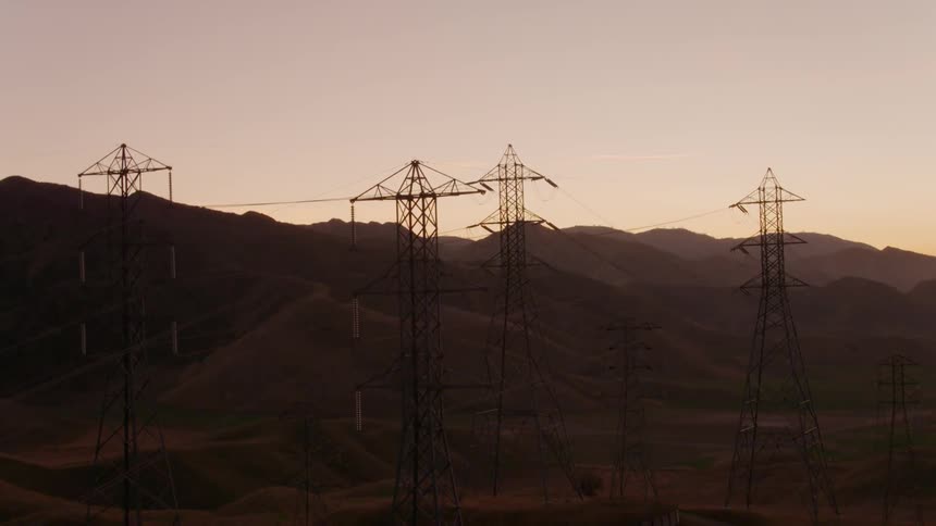 Pullback reveal of numerous power lines and transmission towers against a golden dusk sky