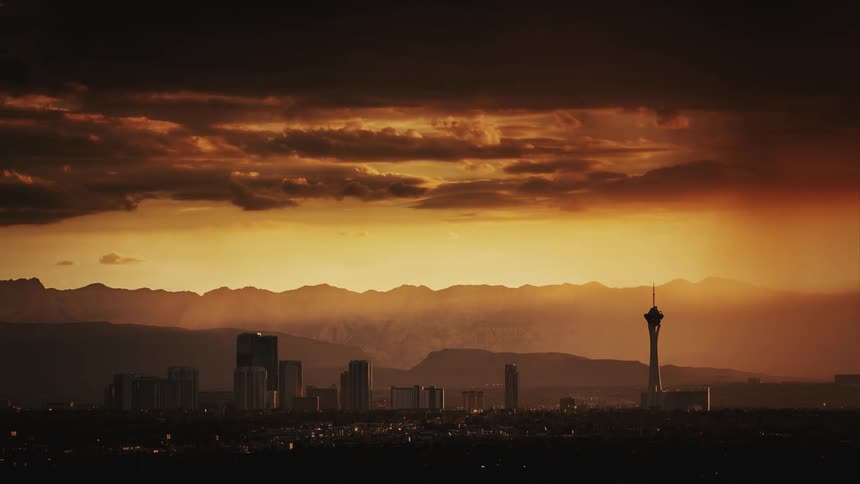 Storm clouds move across and drop rain over a desert city at dusk