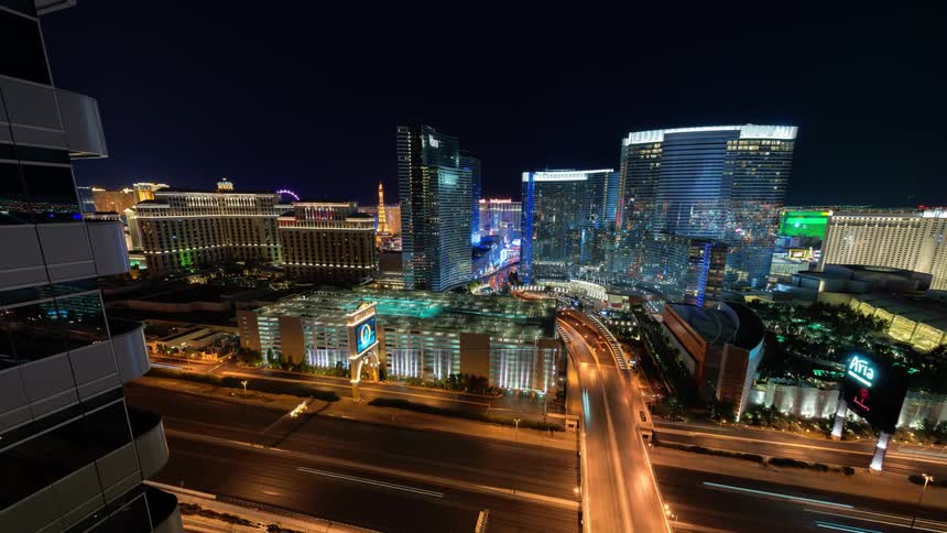 Timelapse of vehicles driving down roads in a brightly lit city at night