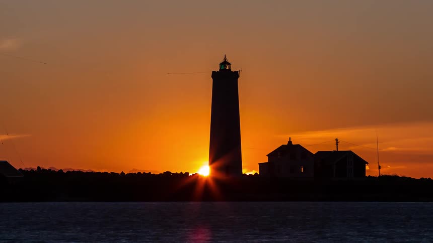The sun sets behind a lighthouse