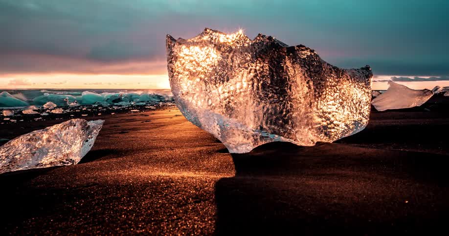 Chunks of clear ice shine as the sun sets on a coastline