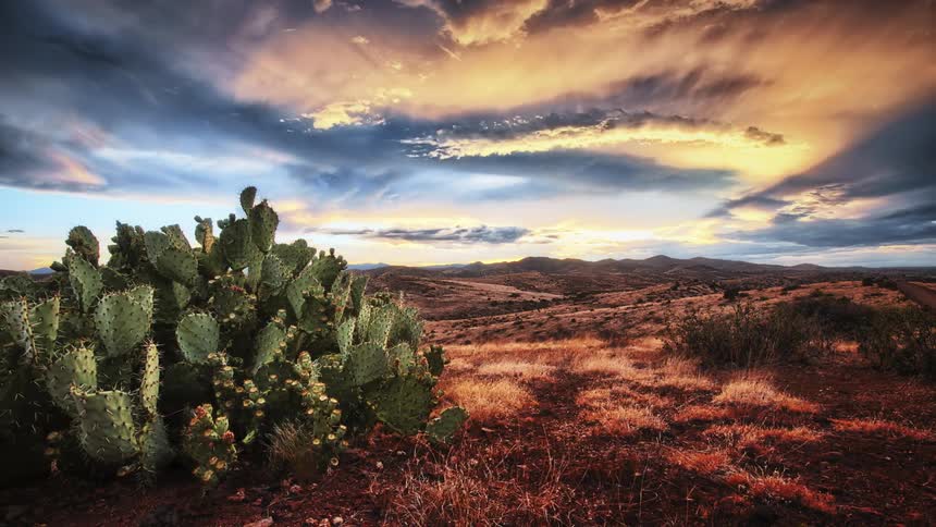 The sun sets as storm clouds roll over a desert landscape