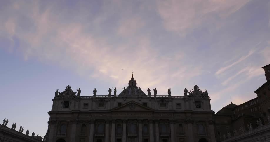 Clouds float above a building with statues at sunset