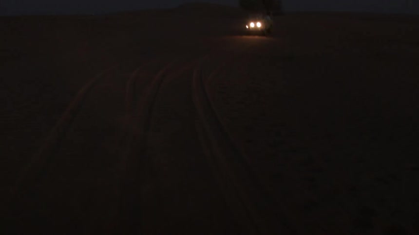 A jeep travels in the desert at night