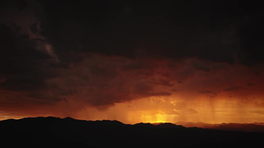 Lightning flashes over distant mountains at sunset