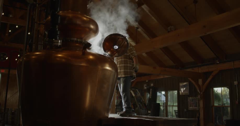 A distillery worker opens up equipment and steam escapes