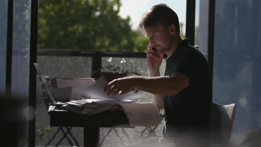 A man talks on a phone while looking through a stack of papers