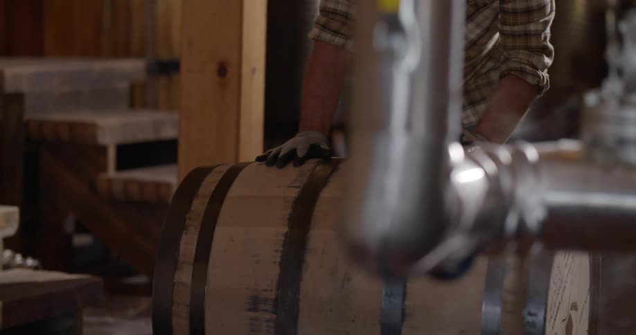 A distillery worker rolls a barrel across the floor