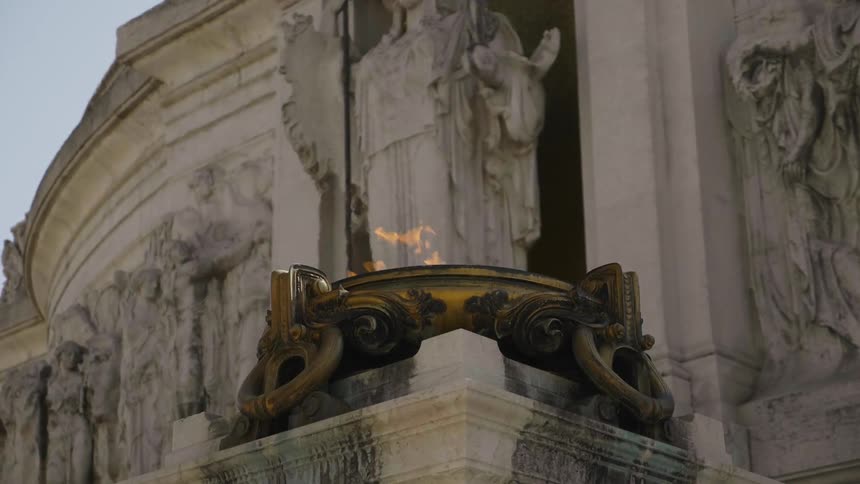 A torch has flames near statues of a building