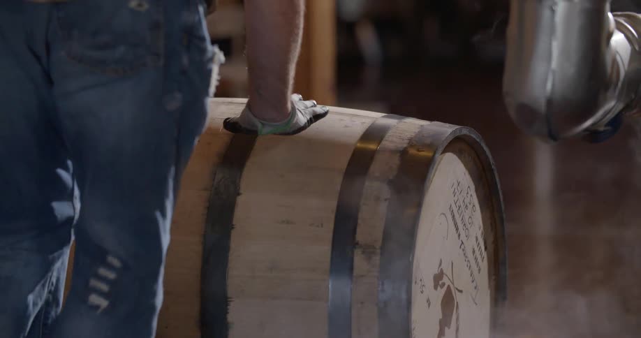 Person wearing gloves rolls a wooden barrel