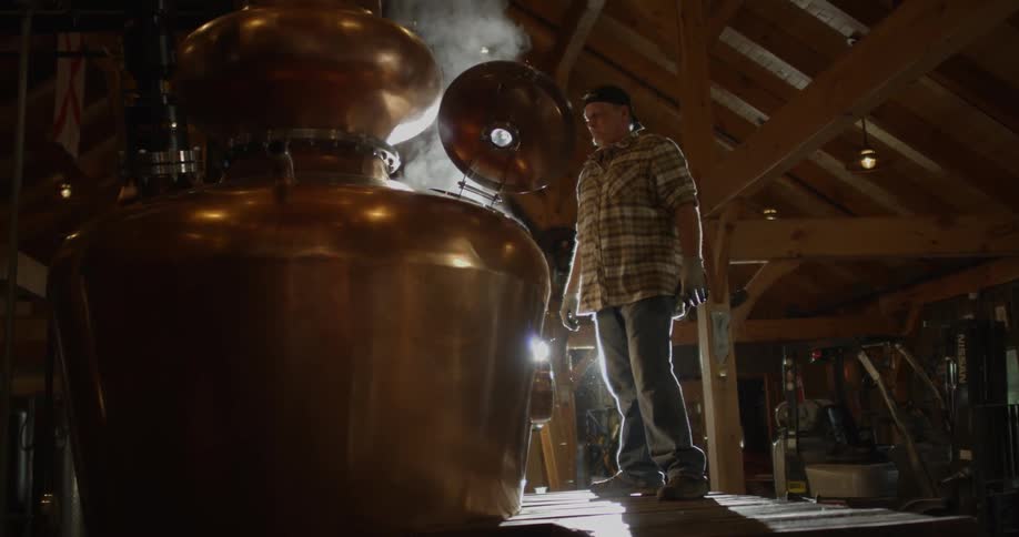 A man stands near large equipment in a distillery