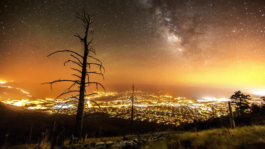 Milky way passes over a brightly lit city.
